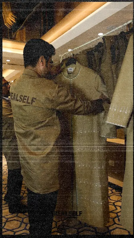 A staff member adjusting a uniform coat on a rack, with a REALSELF garment bag