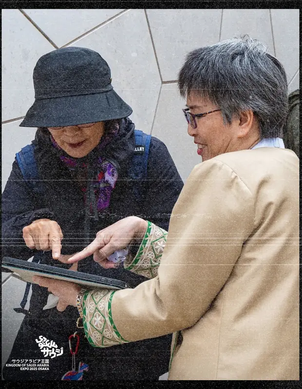 A uniformed host showing a tablet to a visitor, embroidered cuff in view